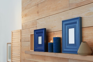 Shelf with burning candles against wooden wall