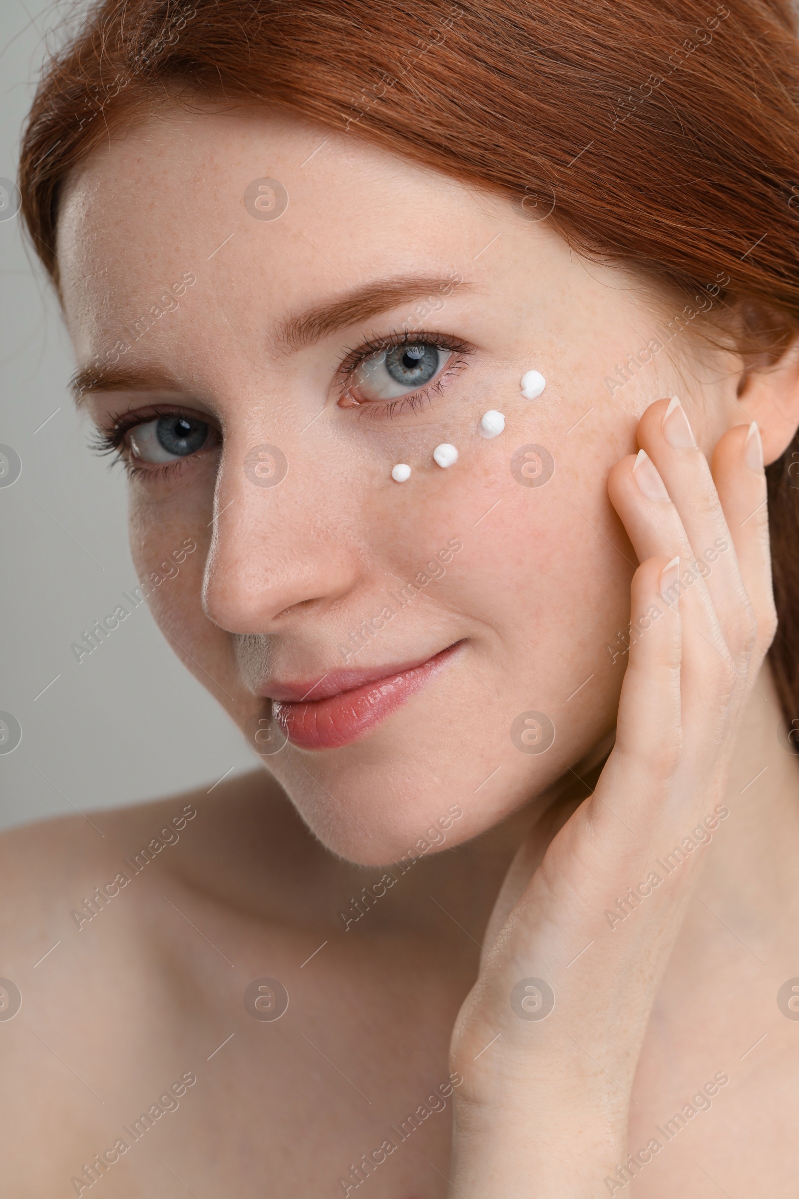 Photo of Beautiful woman with freckles and cream on her face against grey background, closeup