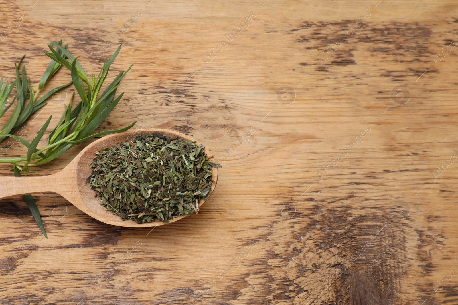 Photo of Spoon of dry tarragon and green leaves on wooden table, flat lay. Space for text