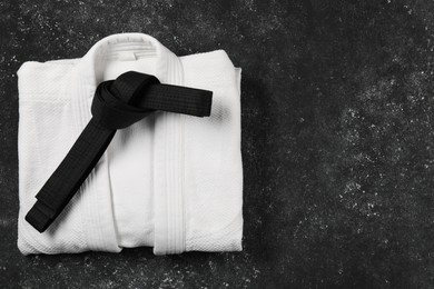 Photo of Black karate belt and white kimono on gray textured background, top view. Space for text