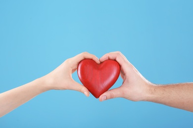 Photo of Man and woman holding decorative heart on color background, closeup