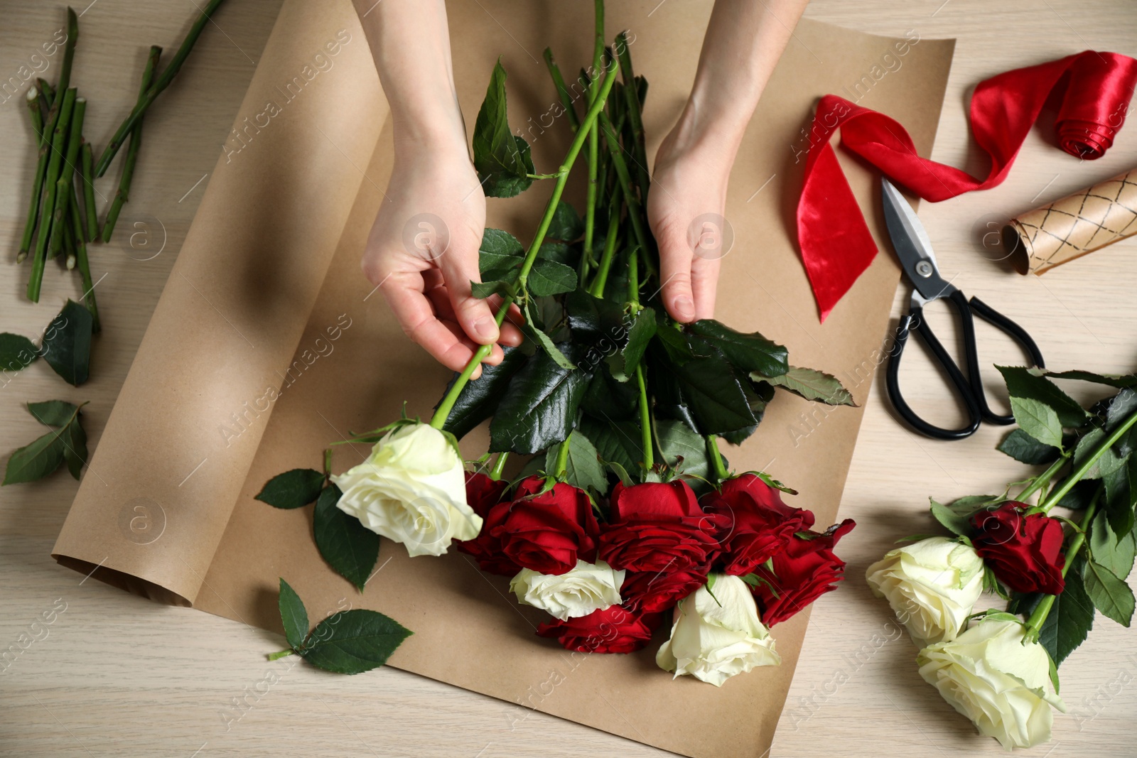 Photo of Woman making luxury bouquet of fresh roses at wooden table, top view