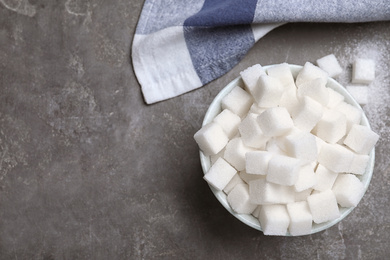 Refined sugar cubes in bowl on grey table, flat lay. Space for text