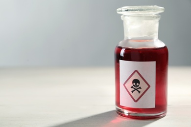 Photo of Glass bottle of poison with warning sign on light background, closeup. Space for text
