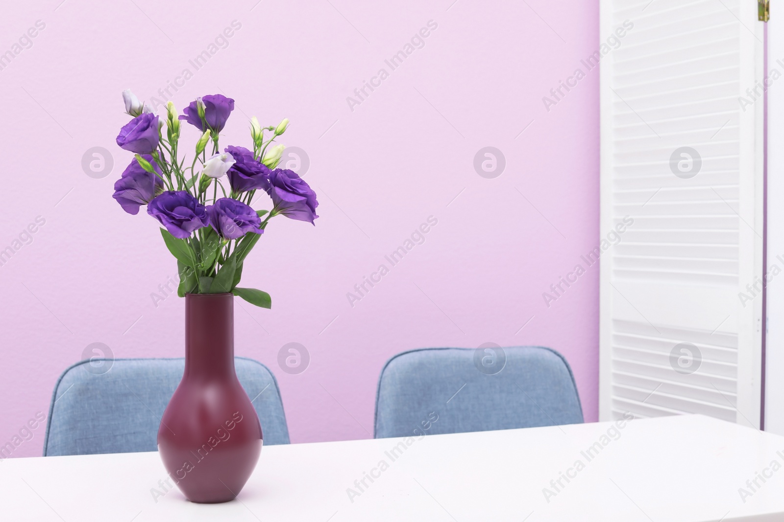 Photo of Beautiful bouquet in vase on white table against color background. Stylish interior