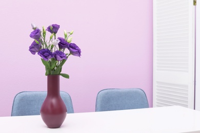 Photo of Beautiful bouquet in vase on white table against color background. Stylish interior