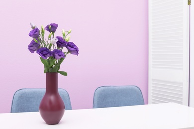 Beautiful bouquet in vase on white table against color background. Stylish interior