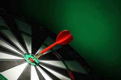 Photo of Red arrow hitting target on dart board against green background. Space for text