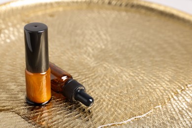 Photo of Bottles with oil on wet golden plate, space for text. Natural cosmetics