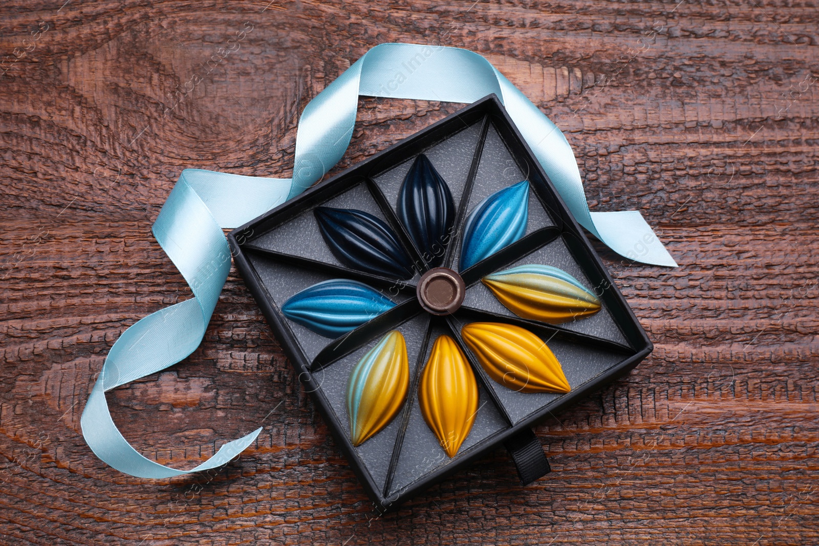 Photo of Box of tasty chocolate candies and ribbon on wooden table, flat lay