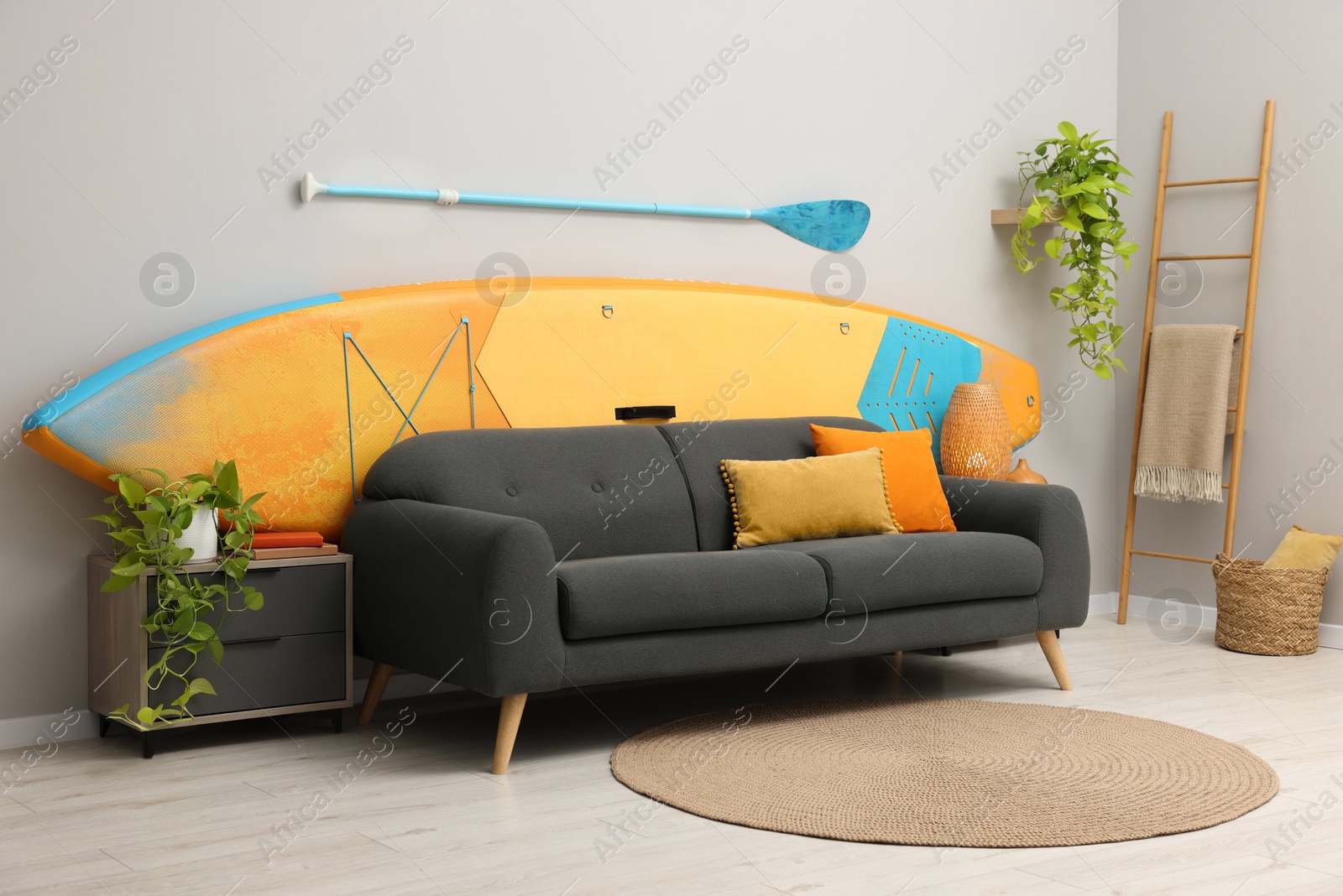 Photo of SUP board, paddle and stylish sofa in living room. Interior design