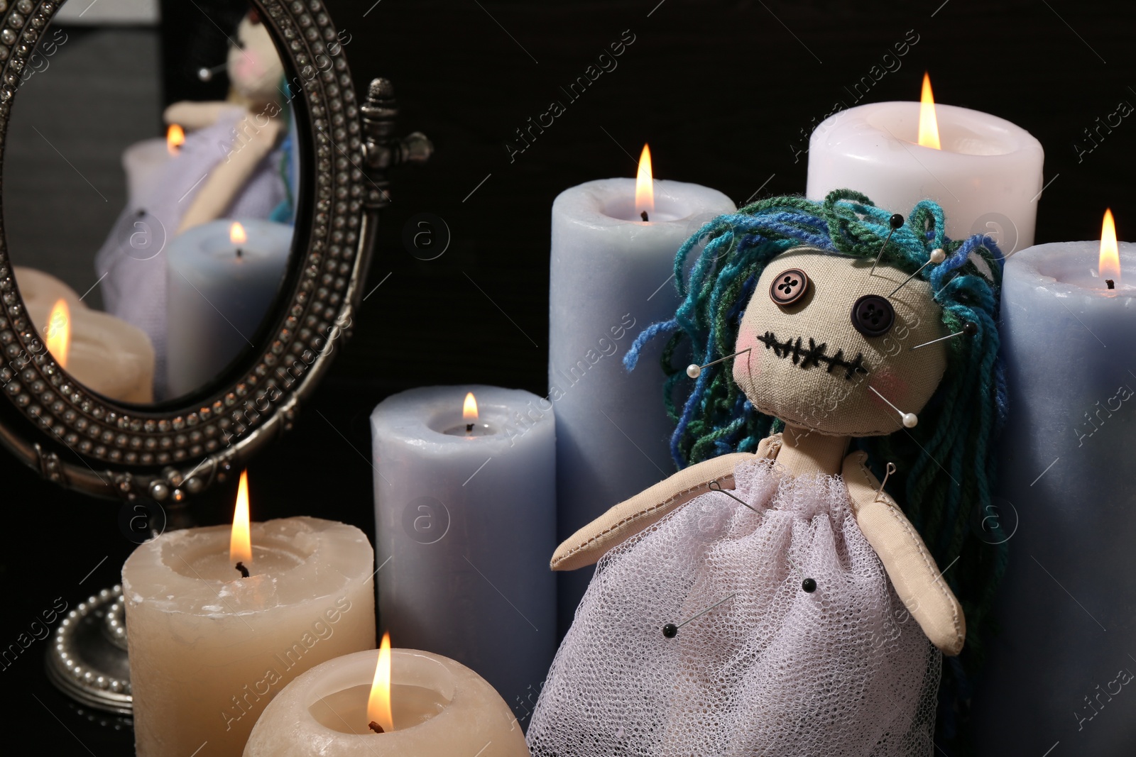 Photo of Voodoo doll pierced with pins and candles on black background. Curse ceremony