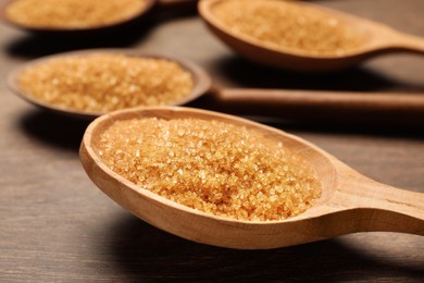 Photo of Spoons with brown sugar on wooden table, closeup