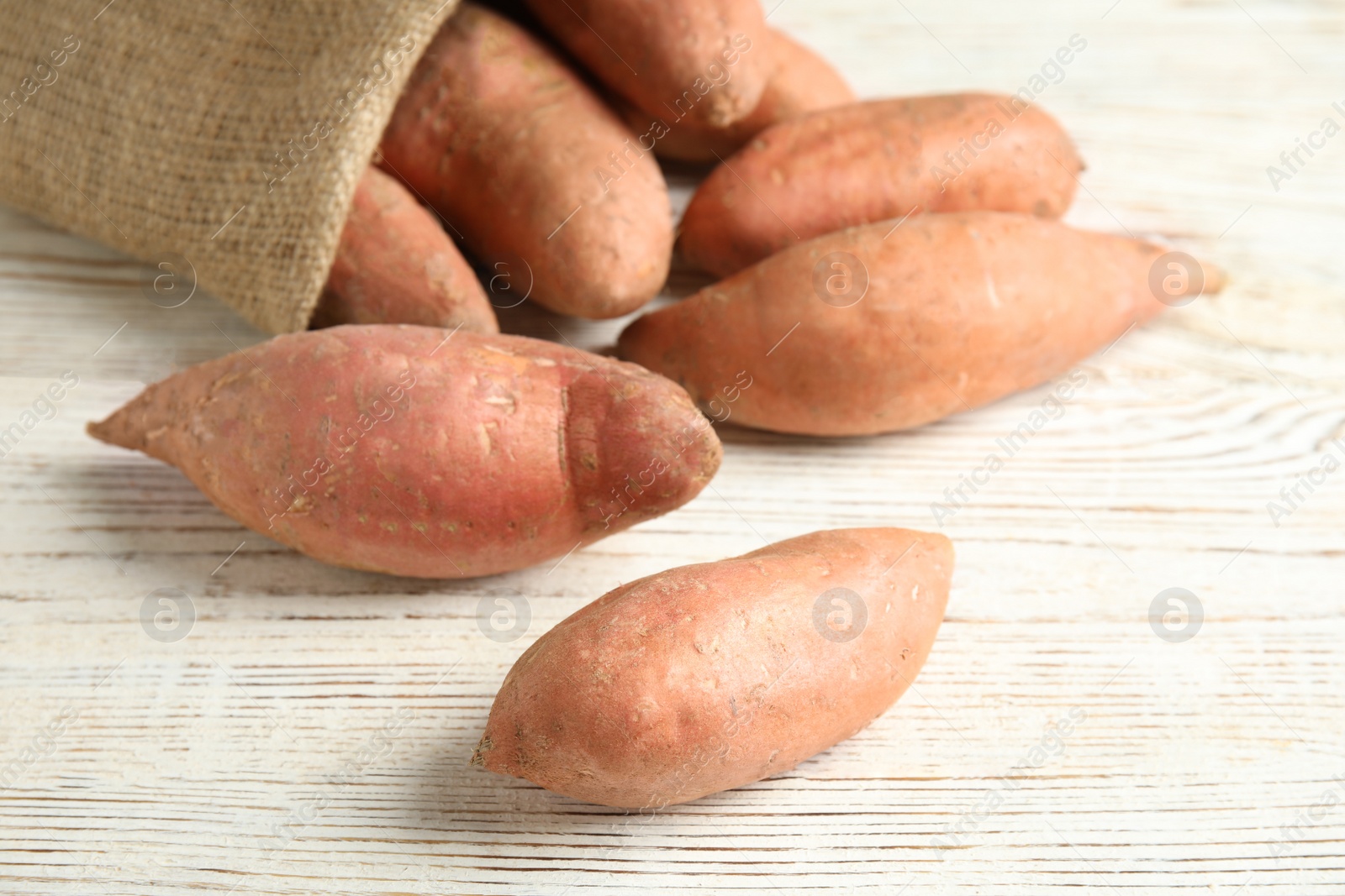 Photo of Ripe sweet potatoes and sackcloth bag on white wooden table