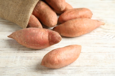 Photo of Ripe sweet potatoes and sackcloth bag on white wooden table