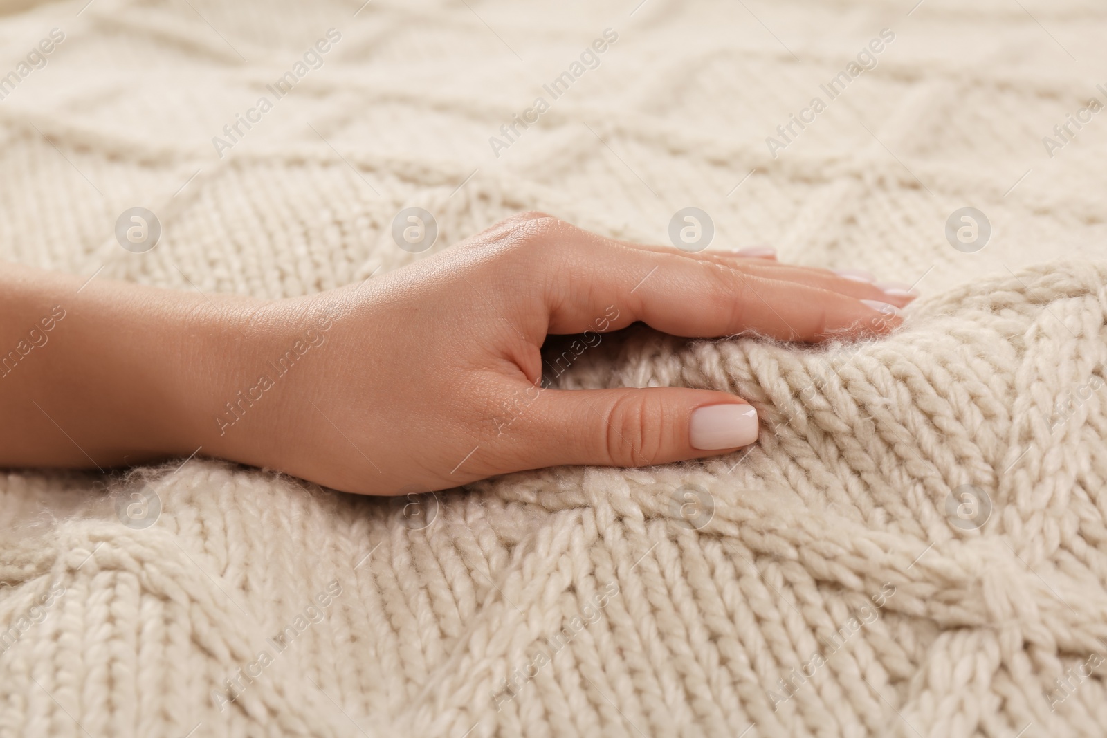 Photo of Woman touching soft beige knitted fabric, closeup