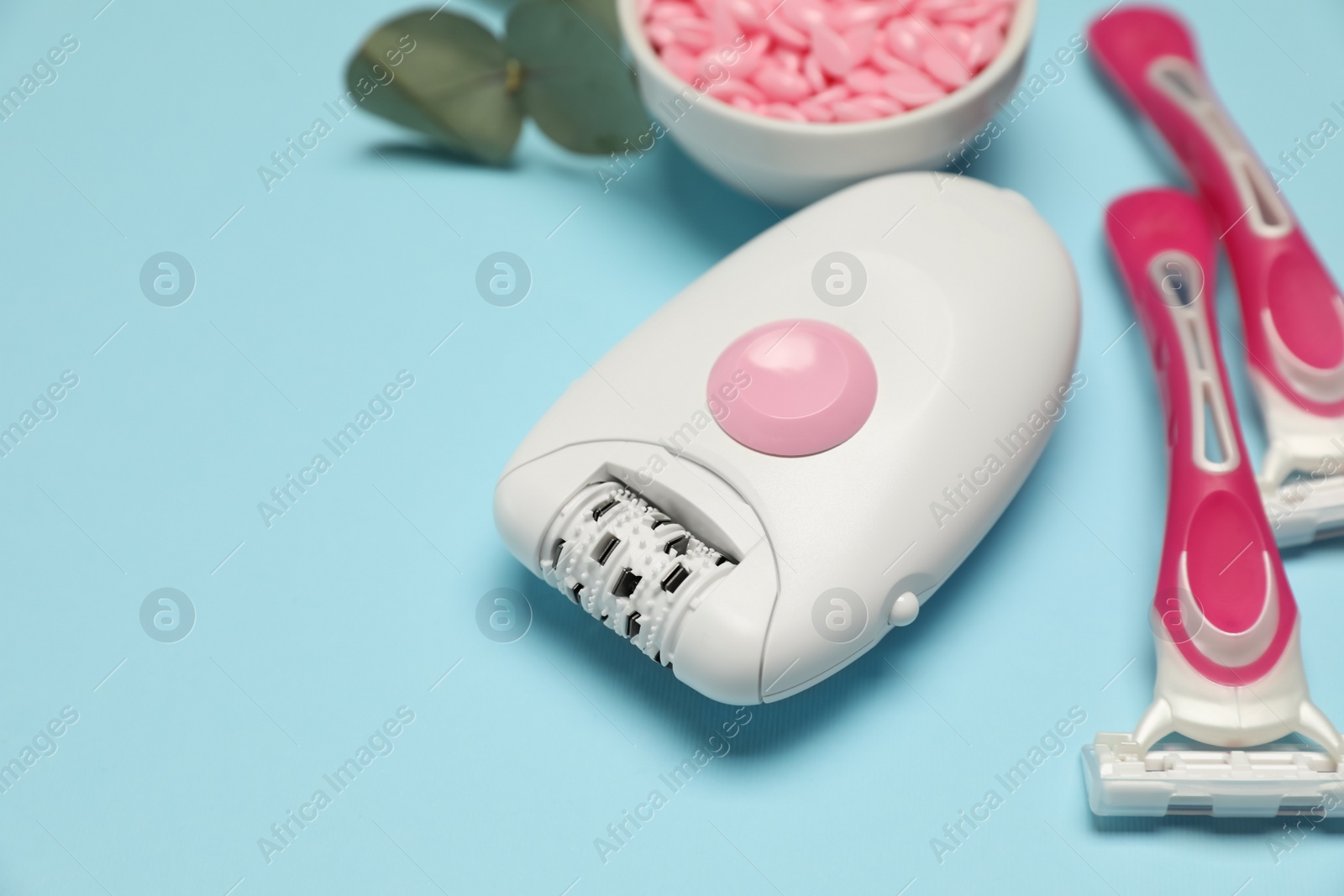 Photo of Epilator, razors and wax beads on light blue background