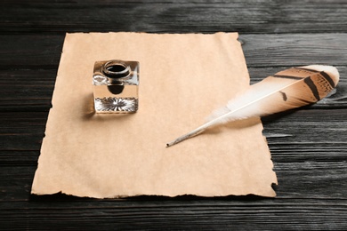 Feather pen, inkwell and blank parchment on wooden table