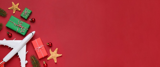 Image of Flat lay composition with toy airplane, gift boxes and space for text on red background. Christmas vacation