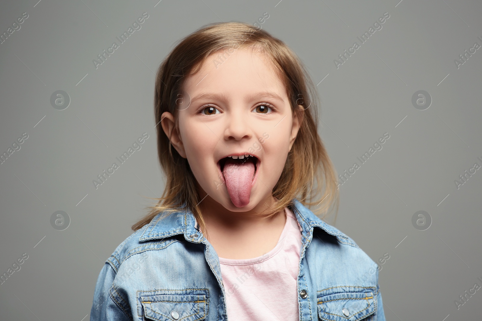 Photo of Emotional little girl showing her tongue on grey background