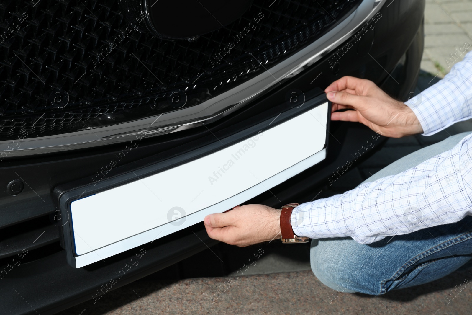 Photo of Man installing vehicle registration plate outdoors, closeup