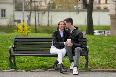 Photo of Lovely young couple with cups of coffee on bench outdoors. Romantic date