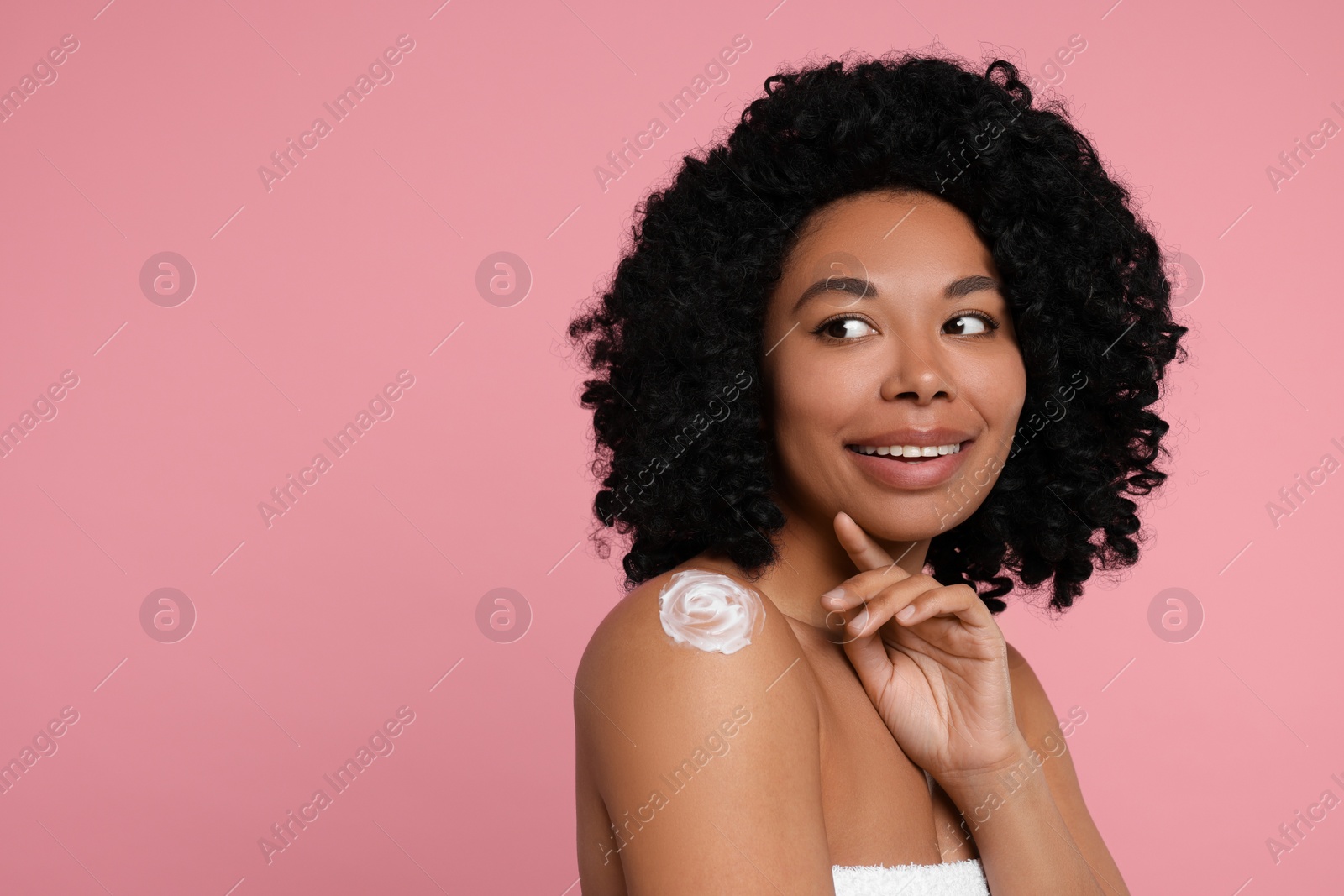 Photo of Young woman applying body cream onto shoulder on pink background. Space for text