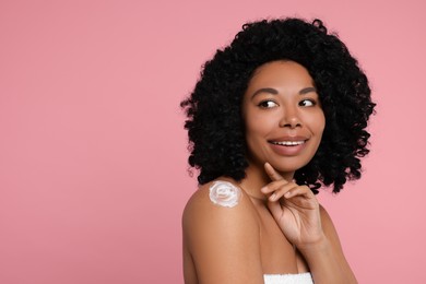 Photo of Young woman applying body cream onto shoulder on pink background. Space for text