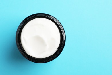 Jar of face cream on light blue background, top view. Space for text