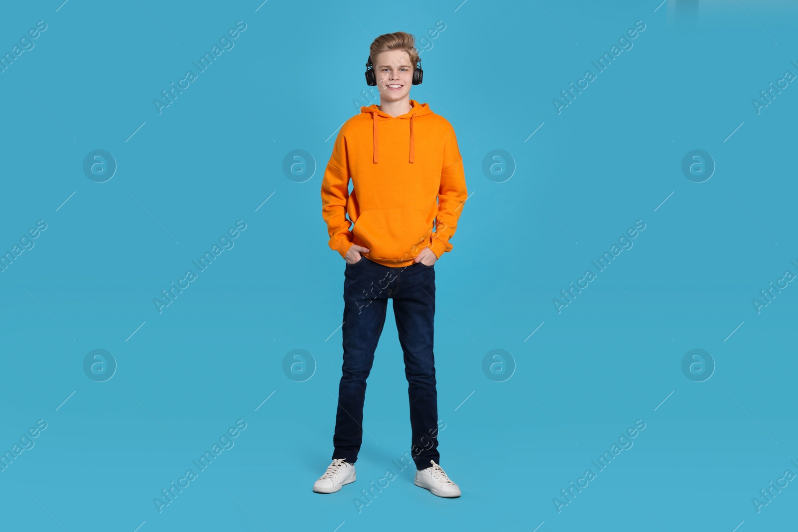 Photo of Teenage boy listening to music with headphones on light blue background