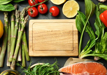 Flat lay composition with asparagus, products and wooden board on black table, space for text