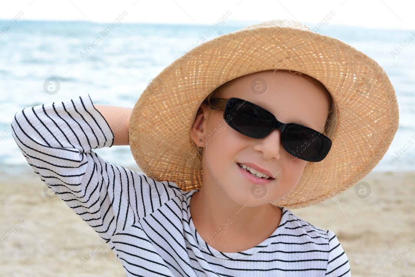 Photo of Little girl wearing sunglasses and hat at beach on sunny day