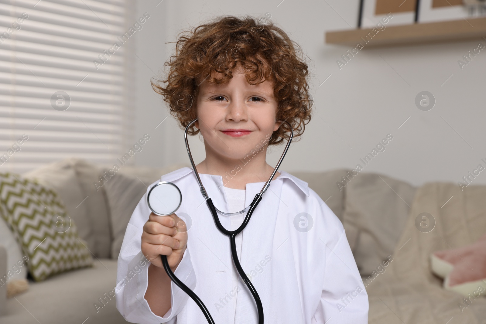 Photo of Little boy in medical uniform with stethoscope at home