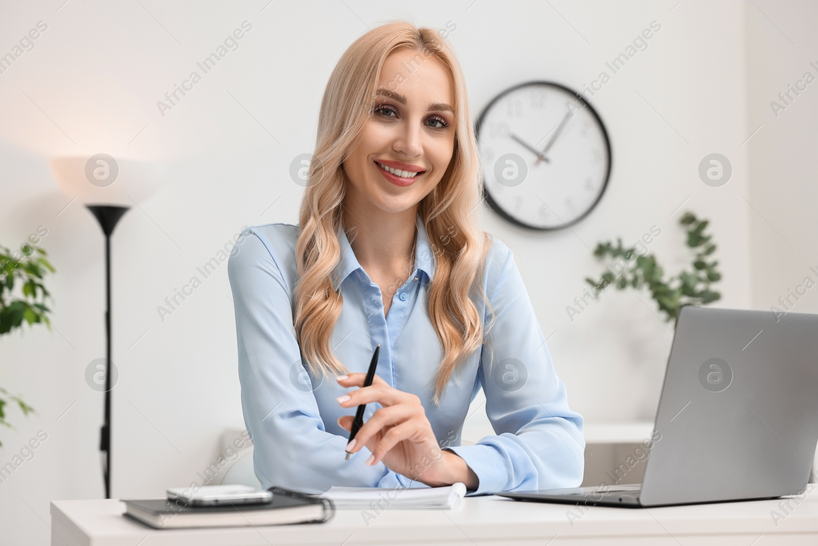 Photo of Happy secretary at table with laptop and stationery in office