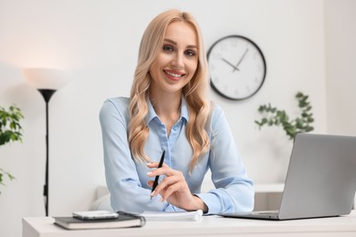 Happy secretary at table with laptop and stationery in office