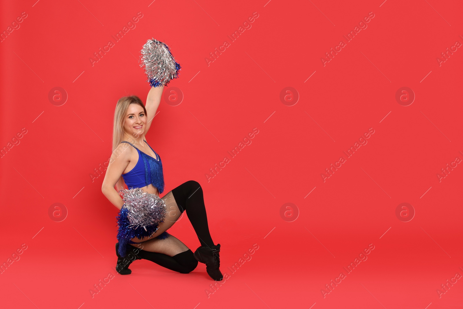 Photo of Beautiful cheerleader in costume holding pom poms on red background. Space for text