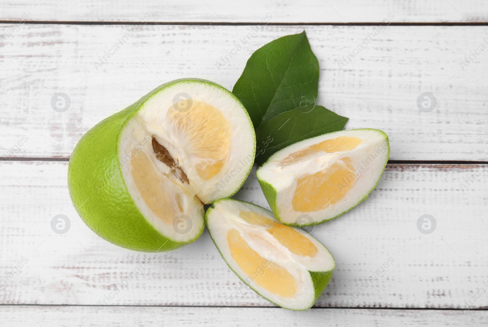 Photo of Cut fresh ripe sweetie fruit with green leaves on white wooden table, flat lay