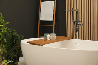 Photo of Spa day. Candles and cosmetic product on wooden tub tray in bathroom