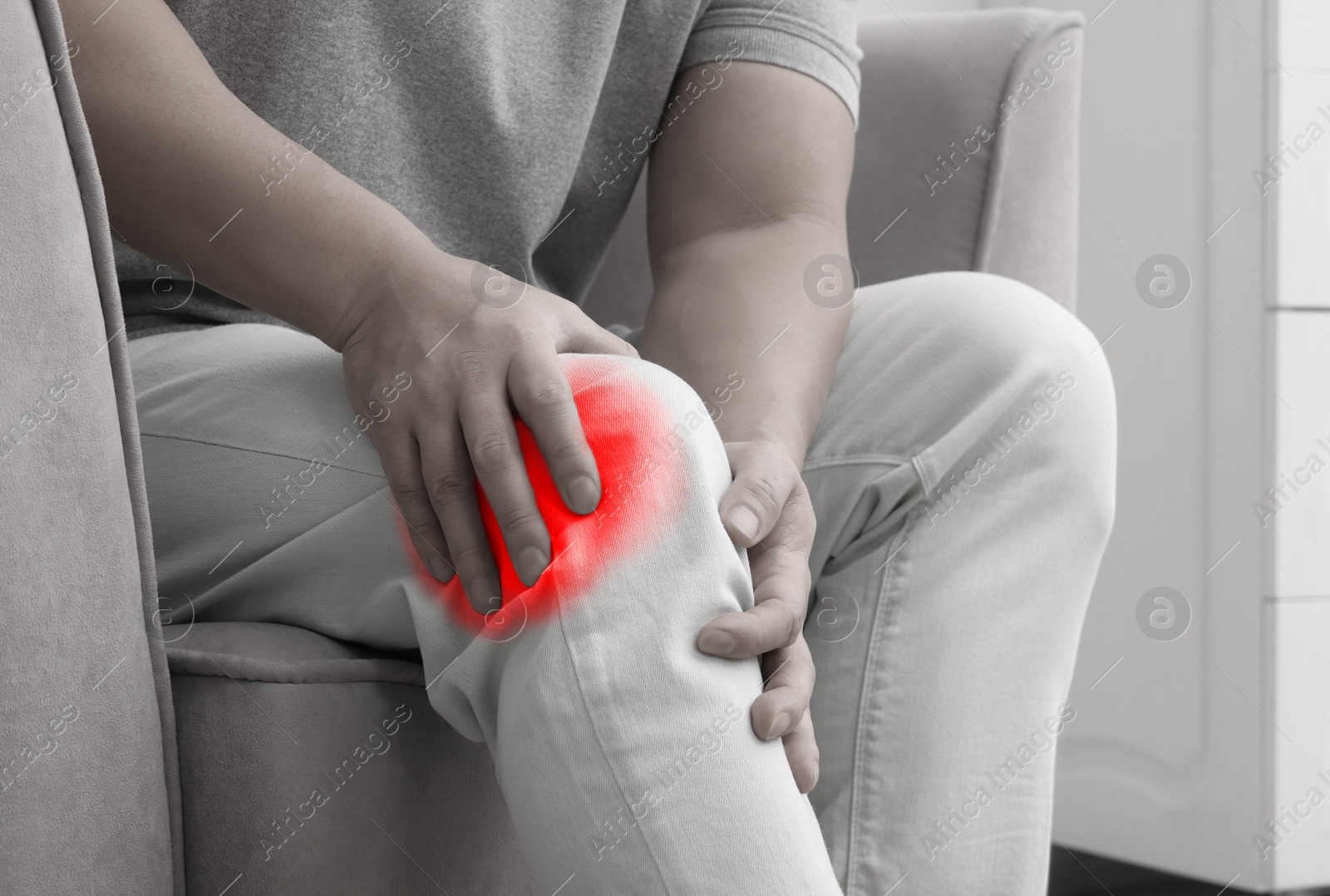 Image of Man suffering from rheumatism on armchair at home, closeup. Black and white effect with red accent in painful area