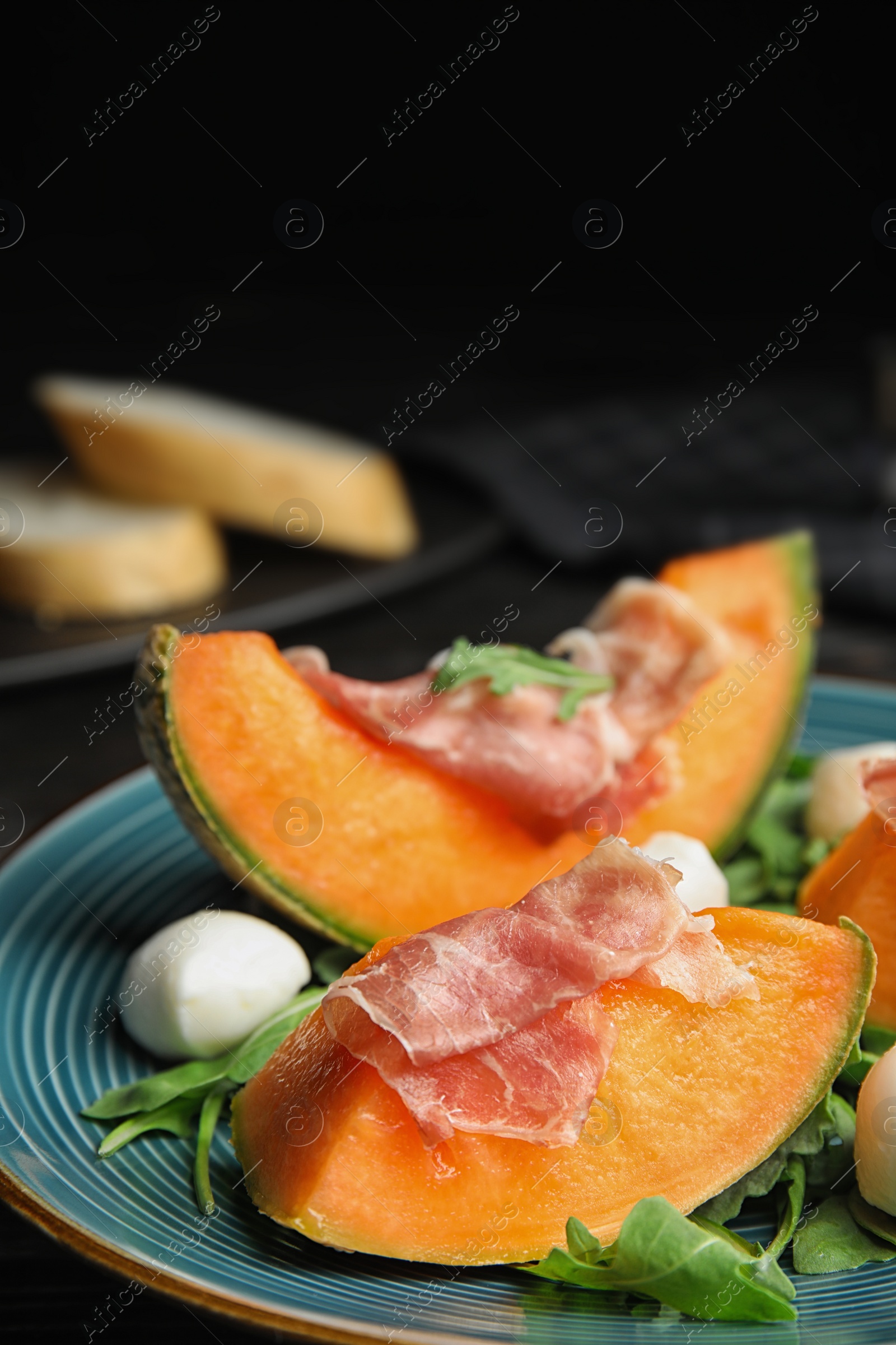 Photo of Fresh melon with prosciutto, mozzarella and arugula on table