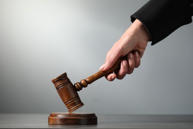 Judge striking mallet at table against grey background, closeup. Space for text