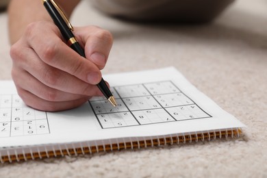 Photo of Man solving sudoku puzzle on floor at home, closeup