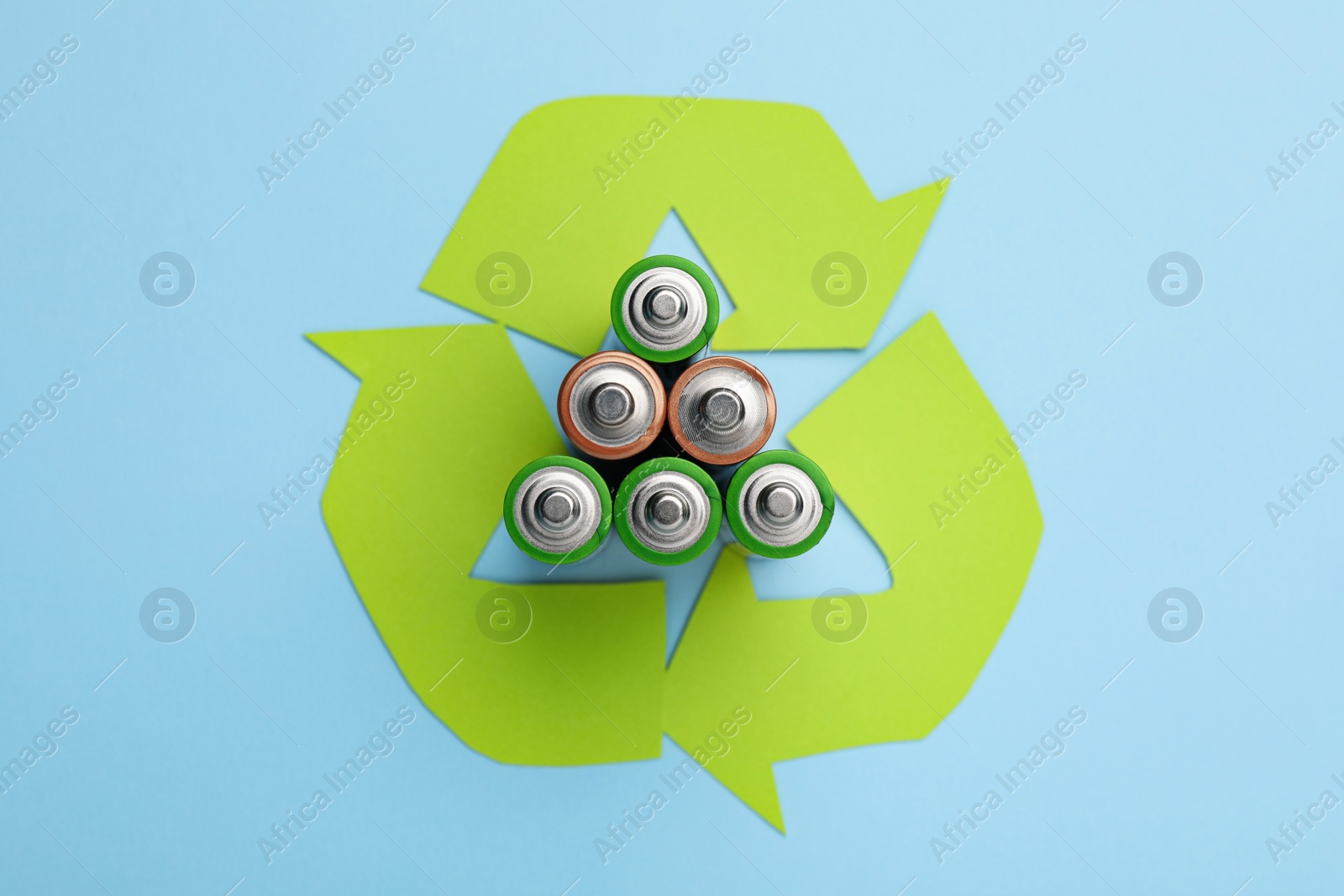 Photo of Used batteries and recycling symbol on light blue background, flat lay