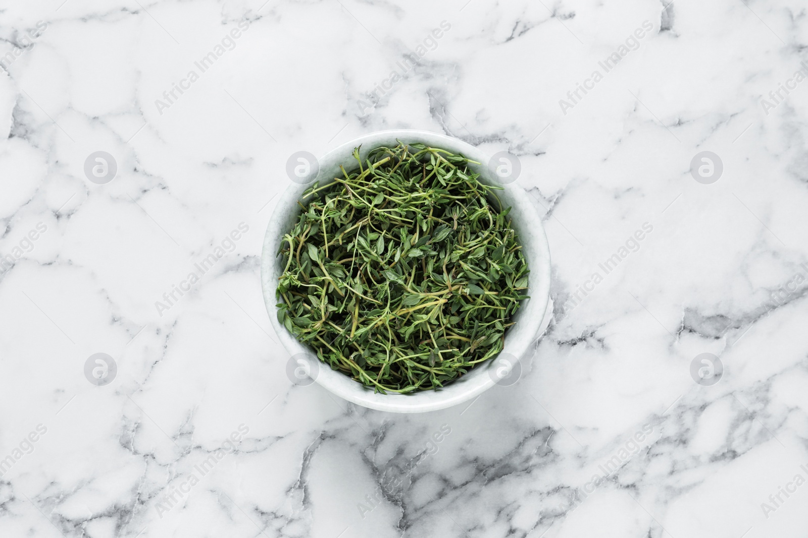 Photo of Aromatic thyme in bowl on white marble table, top view