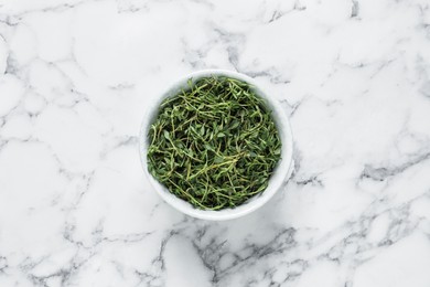 Aromatic thyme in bowl on white marble table, top view