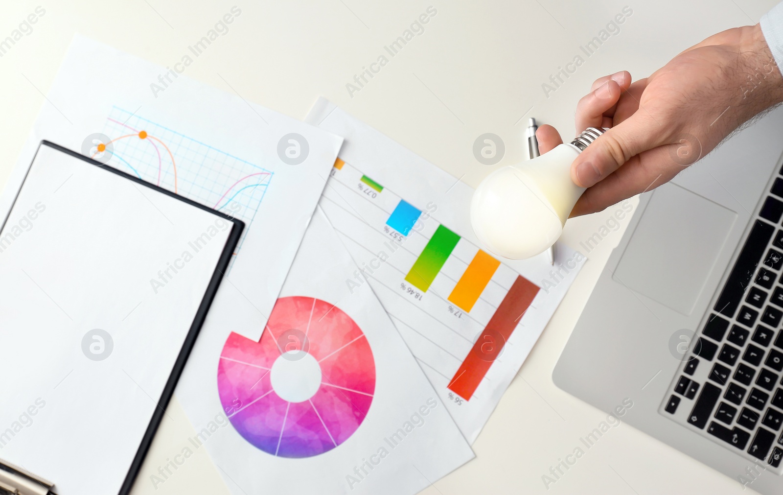 Photo of Man holding lamp bulb over table with laptop and diagrams, top view