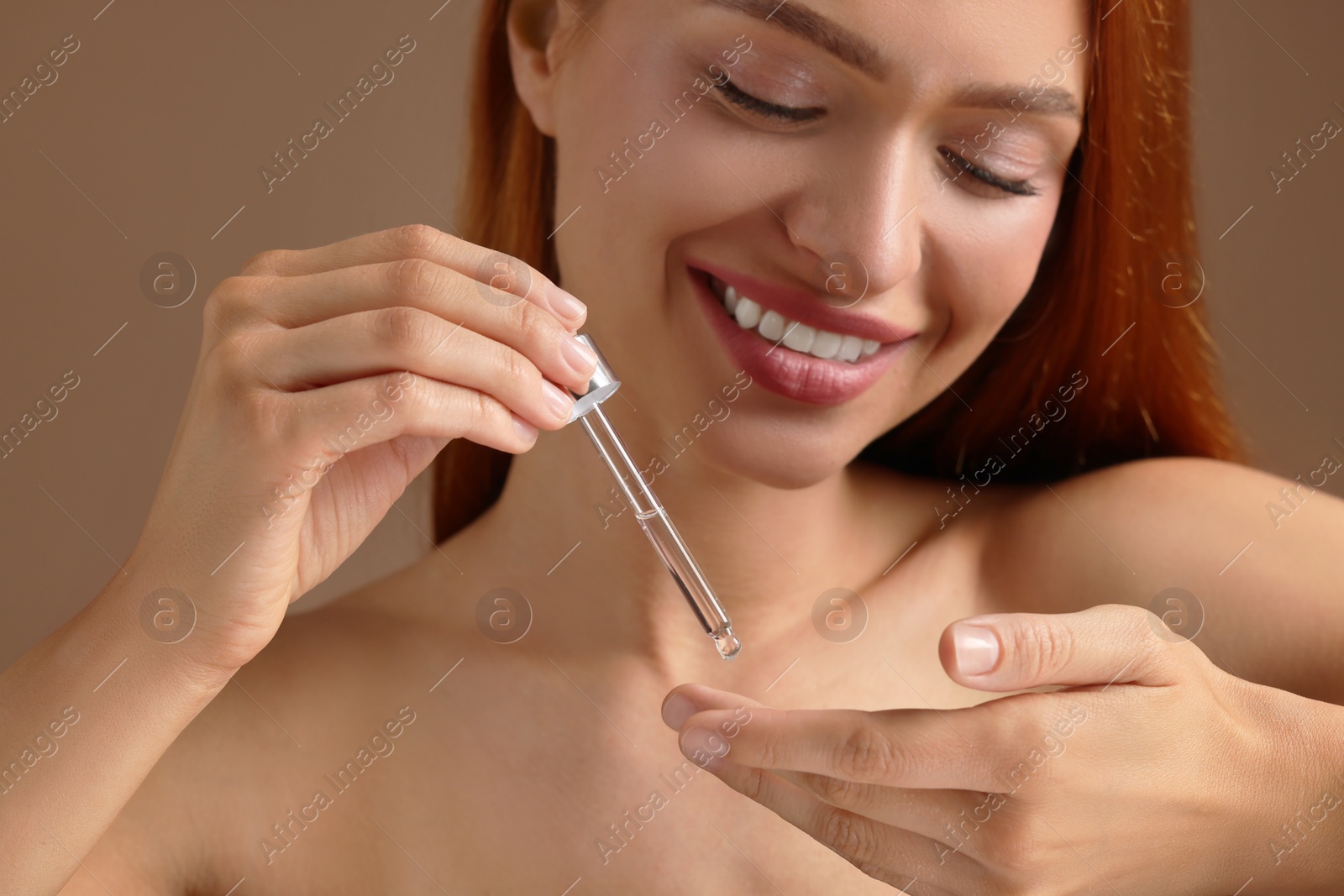 Photo of Beautiful young woman applying cosmetic serum onto her finger on brown background, closeup