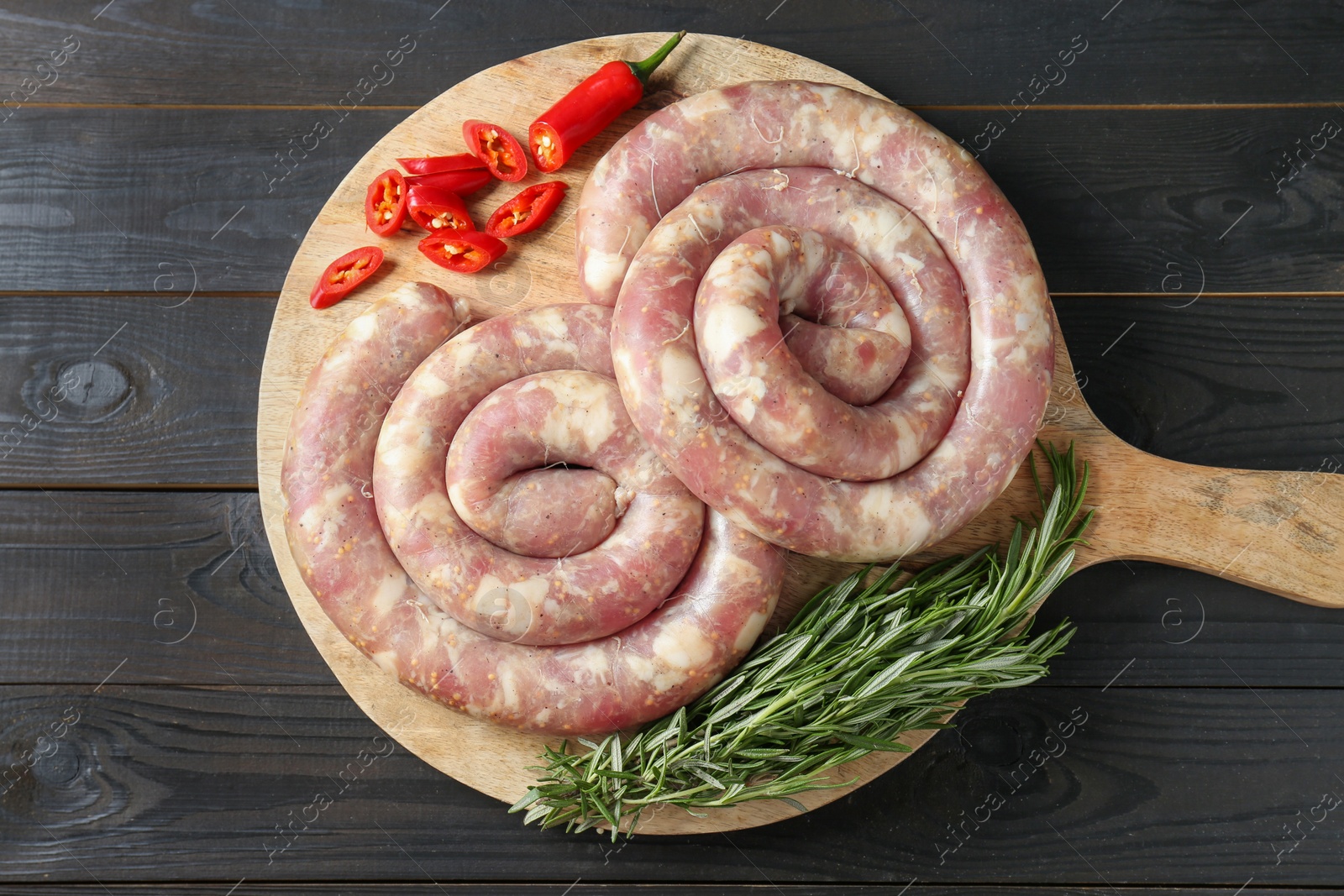Photo of Raw homemade sausage, chili pepper and rosemary on dark wooden table, top view