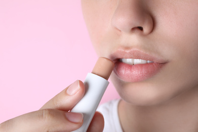 Photo of Woman applying hygienic lipstick on lips against pink background, closeup