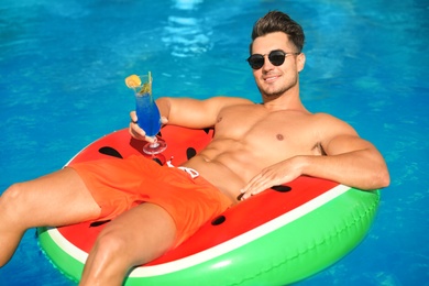 Young man with cocktail and inflatable ring in pool on sunny day